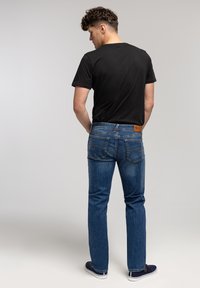 Czarna koszulka z okrągłym dekoltem, niebieskie dżinsy, prosta nogawka, widoczne przeszycia na kieszeniach, brązowa skórzana naszywka w pasie, noszona z granatowymi butami.