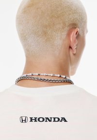 Hvid t-shirt med sort "HONDA" logo på ryggen, lagdelt med sølvkæde- og perlen Halskæder, med glatte og matte teksturer.