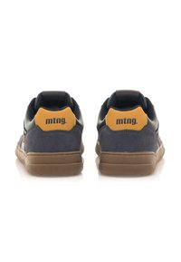 Marinefarbene und braune Wildledersneaker mit einem gelben Fersenelement und schwarzem Logo, mit niedrigem Profil und Gummisohle. Rückansicht gezeigt.