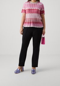 Růžový a bílý úpletový top se zigzag vzorem a krátkým rukávem, spojený s černými kalhotami. Lila boty na bloku a malá růžová kabelka.