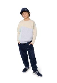 Sweatshirt gris clair et beige avec des blocs de couleur, pantalon cargo en velours côtelé bleu marine et sneakers bleus marines avec le logo "BOSS". Casquette bleue marine assortie.