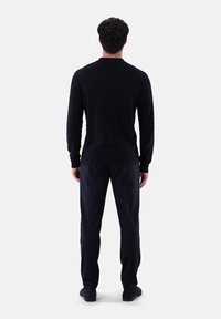 Marineblauer Pullover mit langen Ärmeln und strukturiertem Muster, kombiniert mit dunklen Hosen. Der Pullover hat einen Rundhalsausschnitt sowie gerippte Bündchen und Saum.