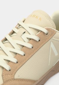 Baskets beiges avec une tige en crème texturée agrémentée d'accents en suède marron, de lacets proéminents et d'un logo sur le côté en bleu clair.