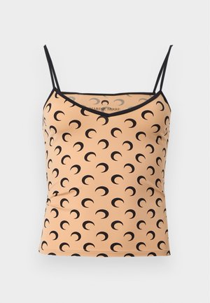 Ung kvinde med langt, lige sort hår iført en beige crop top med sorte halvmåner, sorte bukser og sorte sandaler med høje hæle.