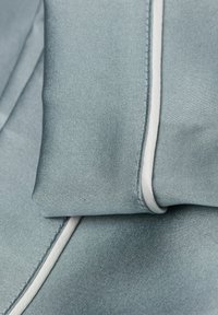 Světle modrá látka s hladkým texturem, s bílým lemováním na jedné straně, uspořádaná v skladech pro jemný vzhled.