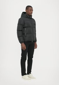 Schwarze Pufferjacke mit Kapuze, mit horizontaler Steppung, Vorderreißverschluss und Seitentaschen. Kombiniert mit schwarzen Hosen und leichten Sneakers.