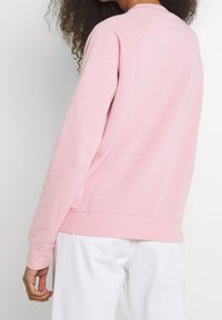 Ljusrosa sweatshirt med långa ärmar, raglanärm, rund halsringning och texturerat tyg, kombinerad med vita byxor.