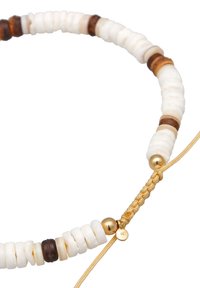 Perlenkette mit weißen und braunen Scheibenperlen, goldenen Akzenten und einem geflochtenen Band mit einem kleinen Anhänger.