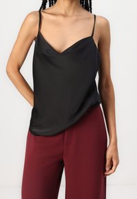 Camisole en satin noir avec un col en V, des bretelles fines et une coupe décontractée, associé à un pantalon bordeaux. Texture lisse et design simple.
