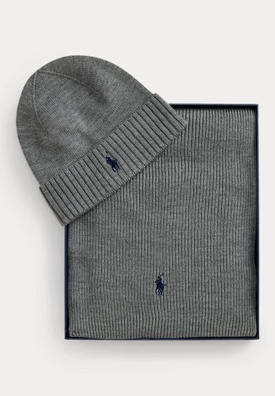 Berretto lavorato a maglia grigio e sciarpa abbinata con piccolo logo scuro, ordinatamente disposti in una scatola rettangolare su sfondo bianco.