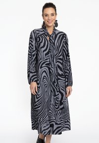 Schwarz-weiß gestreiftes Kleid mit Schleifenkragen, langen Ärmeln und plissierter Textur, das bis zur Mitte der Wade reicht. Getragen mit schwarzen Schuhen.