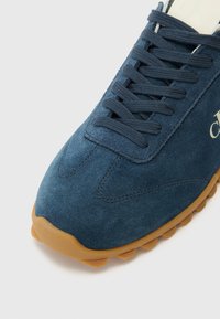 Dark blue suede sneaker with brown rubber outsole, featuring flat laces and reinforced stitching detail. Logo embossed on side.