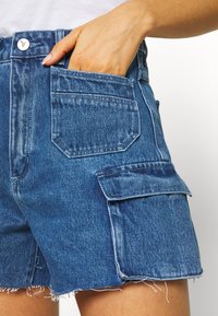 Jeansshorts i medelblått med en blekt finish, med fransad fåll, sidoficka och bakfickor. Knappstängning vid midjan.