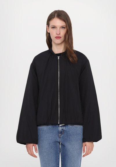 Giubbotto bomber nero con zip frontale, colletto rotondo e maniche ampie. Realizzato in tessuto leggero, presenta un orlo leggermente arricciato.