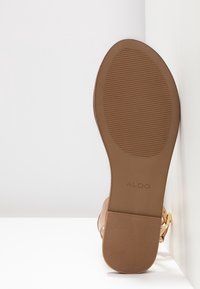 Semelle d'une sandale beige avec une prise texturée et le nom de la marque ALDO, montrant un talon plat et une bride de cheville avec une boucle dorée.