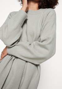 Maglione grigio chiaro realizzato in un tessuto morbido, con collo a girocollo a coste e maniche a palloncino, dalla vestibilità rilassata che cade delicatamente in vita.