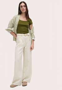 Olivgrön figurnära topp kombinerad med en randig skjorta med krage, vida krämfärgade byxor med skärp och beigefärgade slip-ons.