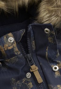Marinblå jacka med ett mönstrat yttre, med en fuskpäls huva, dragkedja och metallknappar. Strukturerad tyg med fiskbensdesign.