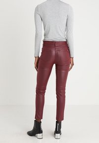 Persona que lleva pantalones de cuero burdeos ajustados, una camiseta de manga larga gris claro y botas negras hasta el tobillo con tacones de bloque plateados, visto desde atrás.