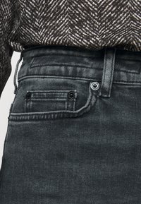 Jeans de denim gris oscuro con un diseño ajustado, que cuentan con un pequeño bolsillo frontal, acentos de botones metálicos y una cinturilla texturizada.