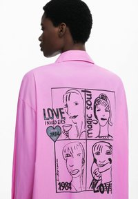 Roze shirt met een losse pasvorm, met een grafisch ontwerp van vier gezichten en de teksten "LOVE INVADERS", "magic soul" en "1984". Gladde stoftextuur.