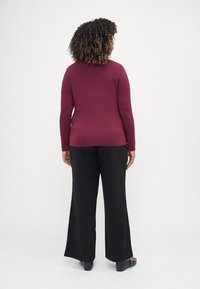 Maroon long-sleeve top paired with black wide-leg pants. The fabric appears smooth with a fitted design accentuating the silhouette.