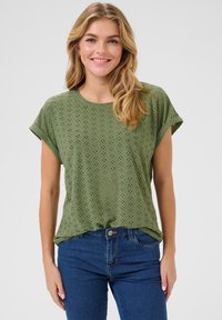 Top corto verde oliva con design traforato a diamante. Abbinato a jeans blu scuro, che presentano una vestibilità comoda e un collo rotondo.