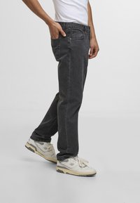 Mørkegrå denimjeans med rett benpassform, fem lommer og en slitt tekstur, parret med lyse joggesko.