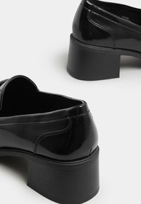 Svarta lackskor med rund design, utrustade med låg klack och subtila sydda detaljer på sidorna.