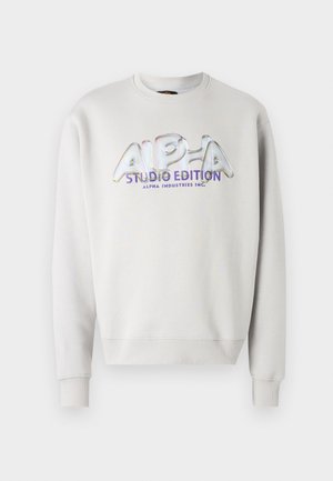 Lys grå hettegenser med en dristig, iriserende trykt logo som leser "ALPHA STUDIO EDITION" i lilla, med ribbestrikkede mansjetter og hals.