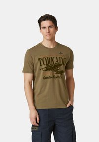 T-shirt in cotone verde oliva con grafica di un aereo nero e testo marrone, colletto rotondo, maniche corte e una vestibilità attillata.