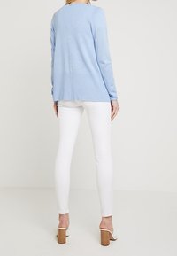 Hellblau, geripptes Langarmoberteil mit rundem Ausschnitt, kombiniert mit weißen Skinny-Jeans und beigen Absatzschuhen.