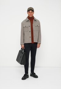 Siva jakna od vune s prednjim džepovima, smešasti turtleneck, crne hlače i crne patike. Drži tanak crni torbu. Karo kapa.