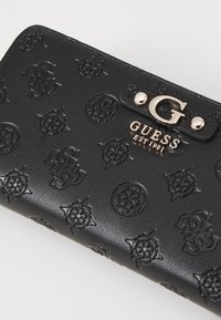Portefeuille noir texturé en simili cuir, arborant des logos et motifs en relief, avec une fermeture à bouton-pression en métal doré.