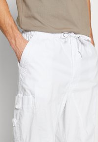 Vita cargo shorts i lättviktsmaterial, med sidofickor och dragsko i midjan. Texturerad detaljering på fickorna.