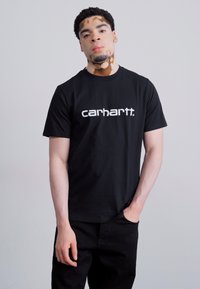 Czarny t-shirt z krótkim rękawem z białym logo "carhartt." na klatce piersiowej. Materiał wydaje się gładki, o klasycznym kroju.