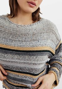 Sweter dzianinowy z okrągłym dekoltem w szare, kremowe i żółte paski. Posiada fakturowany materiał oraz luźne rękawy.
