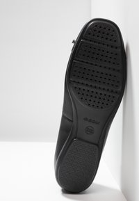 Zapato de cuero negro con suela de goma texturizada y perforaciones, marcado con "GEOX" para mayor transpirabilidad y comodidad.