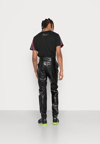 Svart T-shirt med flerfärgade randiga ärmar och signaturdetalj, tillsammans med högmidjade svarta byxor i konstläder och sportiga skor.