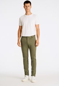 Pantaloni slim fit verde oliva realizzati in morbido tessuto, con chiusura frontale a bottone e tasche laterali. Abbinati a una t-shirt bianca semplice e a sneakers bianche.