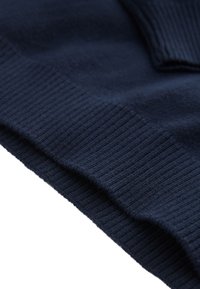 Tissu tricoté bleu foncé avec poignets et ourlet côtelés, montrant en gros plan la texture et les détails des coutures.