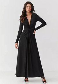 Czarna długa sukienka maxi z długim rękawem, głębokim dekoltem w kształcie litery V oraz skręconym detalem w talii. Gładki, lekki materiał elegancko opada do podłogi.