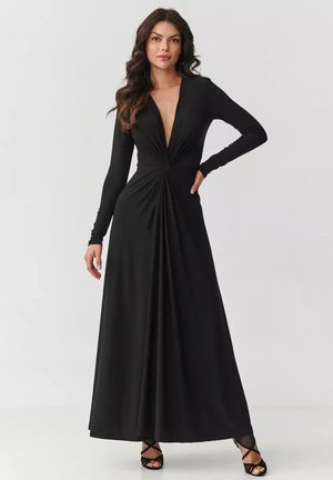 Czarna długa sukienka maxi z długim rękawem, głębokim dekoltem w kształcie litery V oraz skręconym detalem w talii. Gładki, lekki materiał elegancko opada do podłogi.