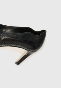 Scarpa nera con tacco alto in materiale sintetico testurizzato, caratterizzata da una stampa a pelle di serpente e da un design elegante con punta affilata e tacco sottile.