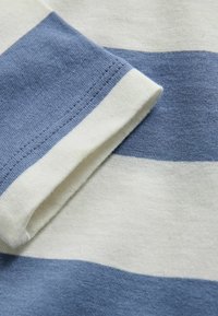 Close-up of folded sleeve on blue and white striped knit fabric, showing detailed stitching and texture.