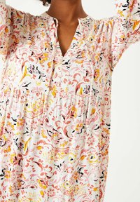 Sukienka w kwiatowy wzór w kolorze białym, z różowymi, żółtymi i czarnymi wzorami. Wykonana z lekkiego materiału, o luźnym kroju i dekolcie w kształcie litery V.