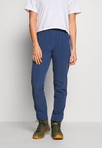 Pantalons légers et bleus pour l'extérieur, fabriqués en tissu résistant, avec une coupe ajustée, des poches latérales, et assortis à des bottes de randonnée vertes.