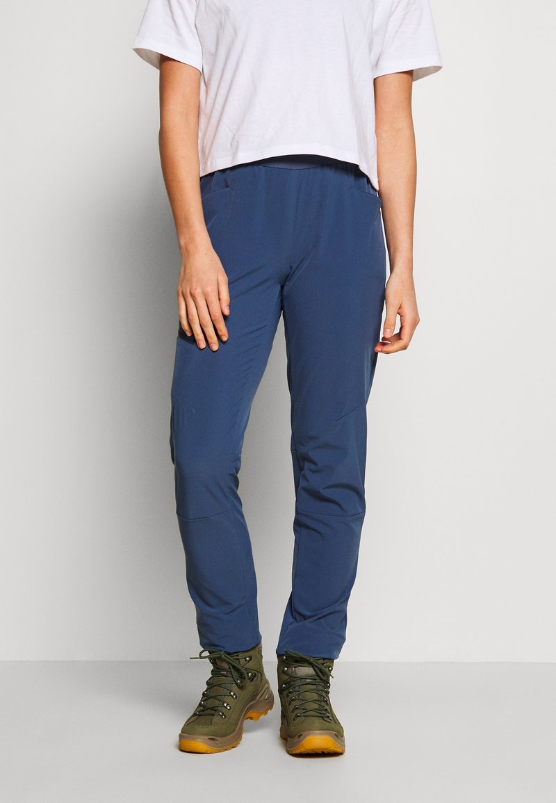 Pantalons légers et bleus pour l'extérieur, fabriqués en tissu résistant, avec une coupe ajustée, des poches latérales, et assortis à des bottes de randonnée vertes.