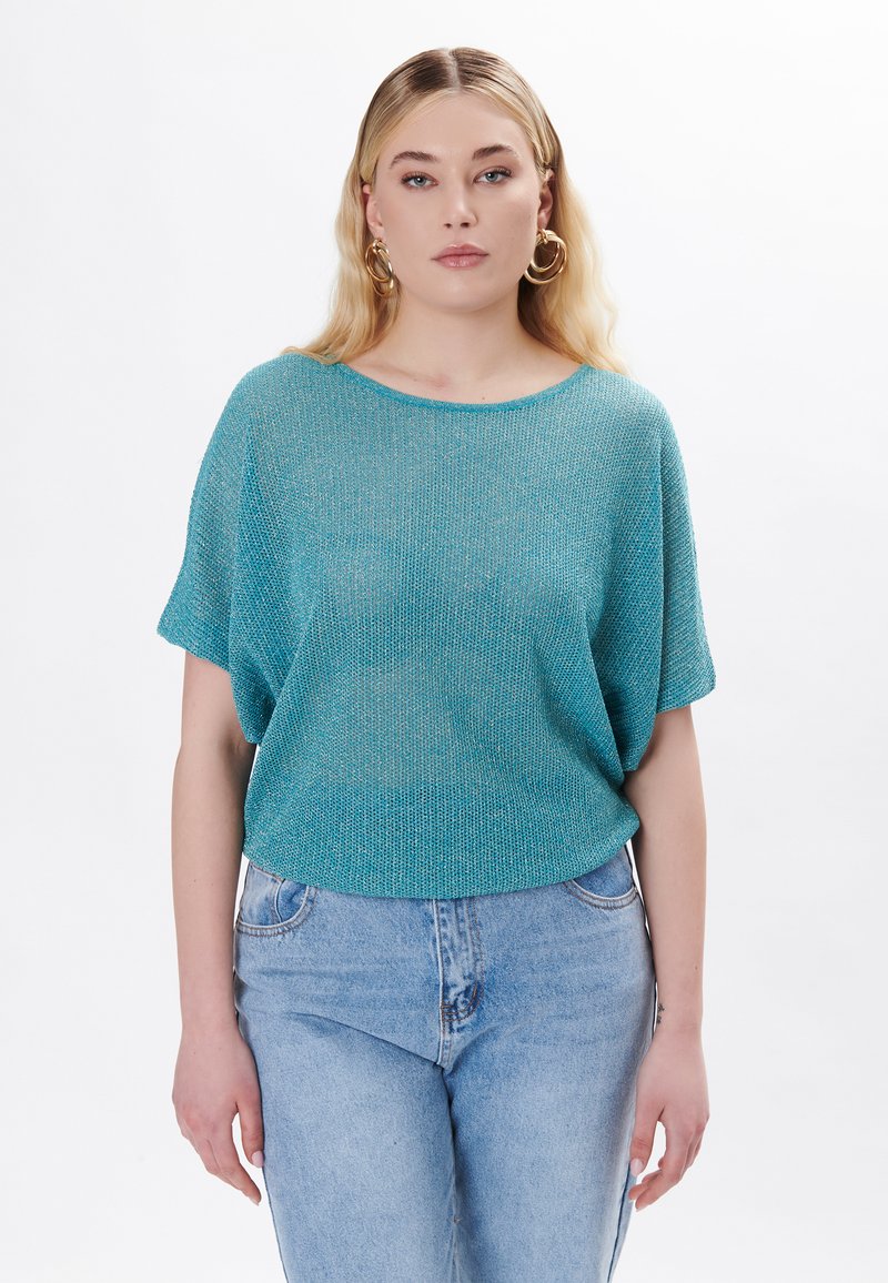 Top de punto turquesa con un diseño holgado y de manga corta. Textura suave, escote redondo, y combinado con jeans de tiro alto de color azul claro.