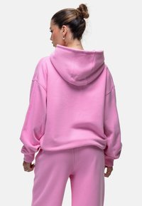 Felpa oversize rosa con tasca a marsupio e cappuccio con lacci. Realizzata in tessuto morbido, presenta spalle scese e polsini a coste.